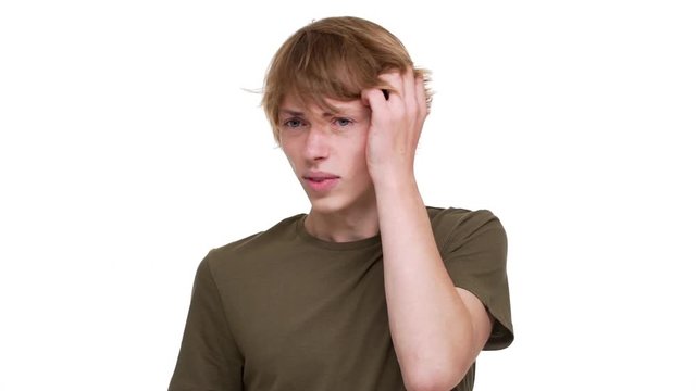 Horizontal portrait of tense blond man grabbing his head being stressed thinking about solution of problem over white wall in slow motion. Concept of emotions
