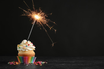 Birthday cupcake with sparkler on table against black background