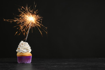 Birthday cupcake with sparkler on table against black background