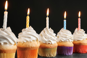 Birthday cupcakes with candles on table against black background