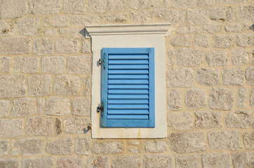 Fototapeta na wymiar Window with blue wooden jalousie on a coastal house facade