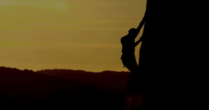 Silhouette of man rock climbing in amazing sunset evening light.
