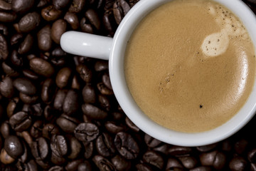 Espresso creamy coffee on a white cup over many brown roasted coffee beans