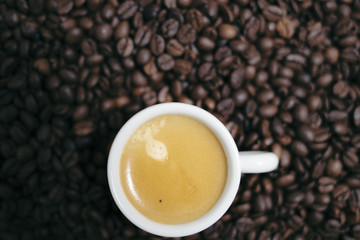 Espresso creamy coffee on a white cup over many brown roasted coffee beans