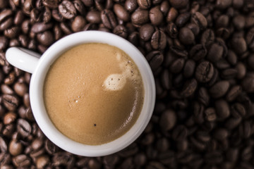 Espresso creamy coffee on a white cup over many brown roasted coffee beans