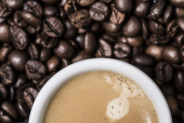 Espresso creamy coffee on a white cup over many brown roasted coffee beans