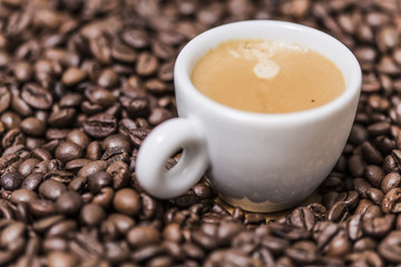 Espresso creamy coffee on a white cup over many brown roasted coffee beans