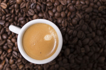 Espresso creamy coffee on a white cup over many brown roasted coffee beans