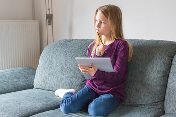 Ein Mädchen sitz auf dem Sofa und denkt nach mit Stift und Notizblock in den Händen