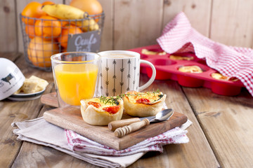 homemade cupcakes with cheese and cherry tomatoes on a wooden board, spoon and knife. table towel in a red cage, a glass of orange juice and fragrant coffee, with space for writing text or advertising