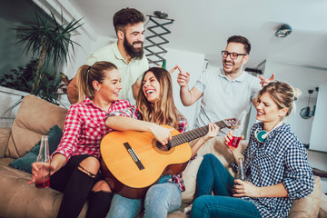 Group of happy young friends having fun and drinking beer in home interior