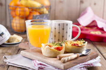 homemade cupcakes with cheese and cherry tomatoes on a wooden board, spoon and knife. table towel in a red cage, a glass of orange juice and fragrant coffee, with space for writing text or advertising