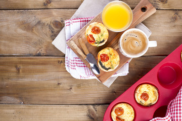 homemade cupcakes with cheese and cherry tomatoes on a wooden board, spoon and knife. table towel in a red cage, a glass of orange juice and fragrant coffee, with space for writing text or advertising