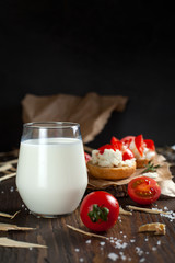 toast with feta cheese on baking paper, a glass of milk, cherry tomatoes and butter on a dark wooden table