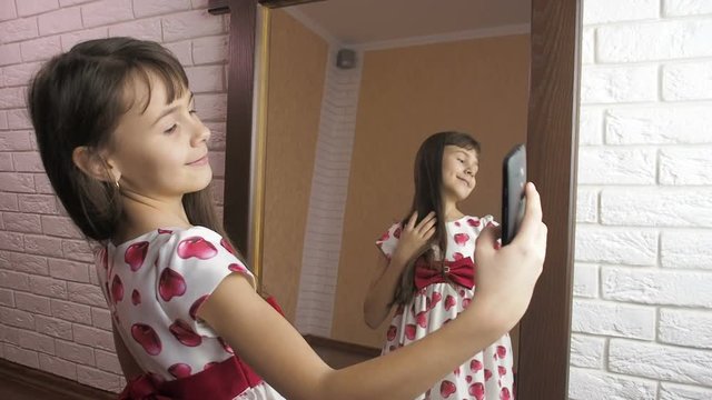 The child takes pictures of himself from the phone. The little girl at the mirror is taking pictures.