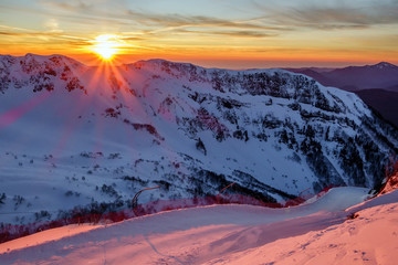 Beautiful scenic winter mountain sunset landscape of snowy Caucasus Mountains and ski slope of...