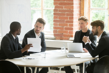 African investment advisor consulting diverse businessmen, partners listening to black consultant holding showing document, making offer, presenting project plan at corporate executive team meeting