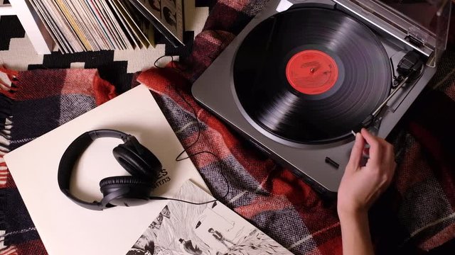 Girl's hand turns on turntable vinyl record player with vinyl records, headphones and plaid on the background
