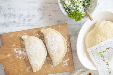 Preparation of homemade pies with cheese and fresh herbs filling. On a wooden board, dough and rolling pin, a towel with a pattern. Free space for text