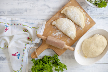 Preparation of homemade pies with cheese and fresh herbs filling. On a wooden board, dough and rolling pin, a towel with a pattern. Free space for text