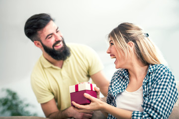 Smiling young man surprising cheerful woman with a gift box at home