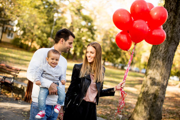 Happy young parents with baby boy in autumn park holding red balloons
