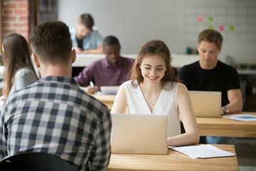 Young smiling woman working on laptop in coworking office, happy employee using computer sitting at...