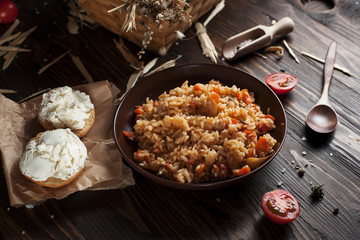 pilaf in a brown ceramic plate, cherry tomatoes, toast with feta cheese and a wooden spoon on a dark wooden table