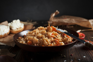 pilaf in a brown ceramic plate, cherry tomatoes, toast with feta cheese and a wooden spoon on a dark wooden table
