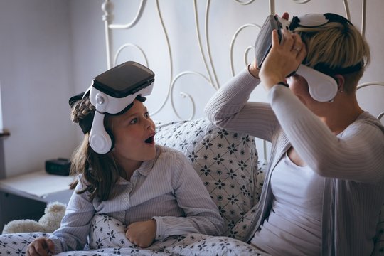 Mother and daughter using virtual reality headset on bed