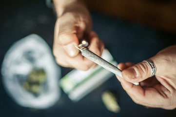 Close up of addict lighting up marijuana joint with lighter - obrazy, fototapety, plakaty