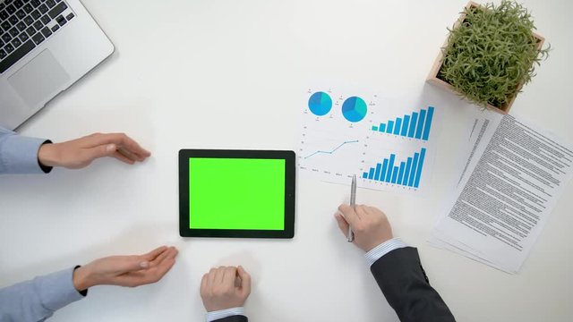 Businessmen analising diagrams in the office. A tablet with a green screen. View from the top of men's hands. Close-up shot.