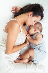Beautiful mother and cute little baby boy sleeping together on bed. 