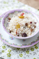 White rice with berries for breakfast, in a plate with a pink pattern. On a tablecloth with flowers.
