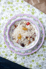 White rice with berries for breakfast, in a plate with a pink pattern. On a tablecloth with flowers.