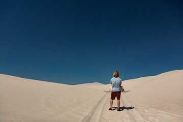 Man with sandboard standing in the desert