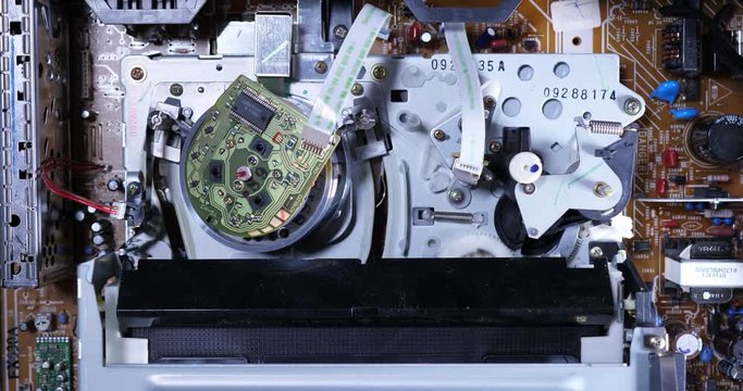 A top-down inside view of the electronics of a VCR as a VHS tape is inserted. Top off view.  	