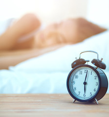 Young sleeping woman and alarm clock in bedroom at home