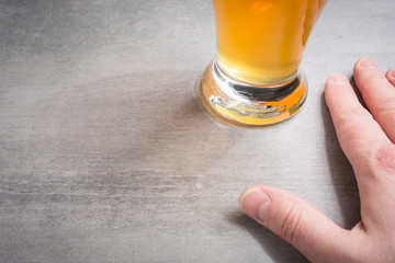 Hand beside a glass of beer on a stone background.
