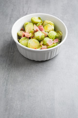 Brussel sprouts and bacon in a white dish on a stone background.