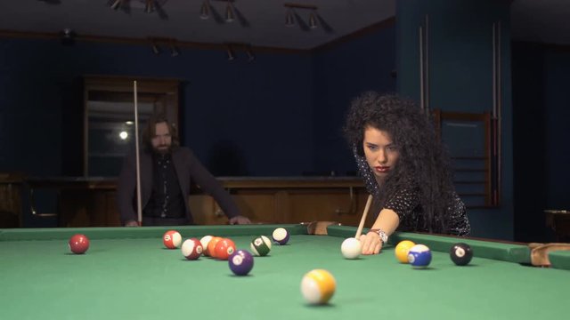 Beautiful sexy woman with red lips hits the billird ball into a pocket