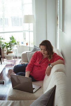 Young pregnant woman sitting on sofa using her laptop