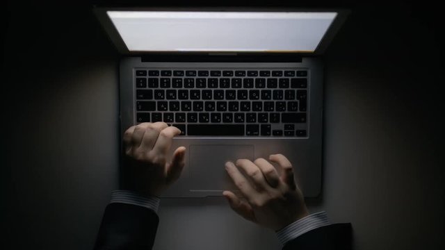 A man's hands working on the laptop at night. The laptop is on the table. View from the top. Close-up shot.