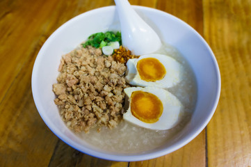 Minced pork congee with egg, fresh ginger and  coriander on white cup and spoon over the wood table.