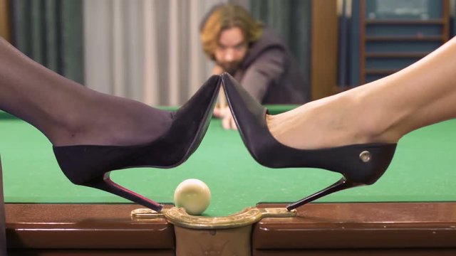 Man get the ball into a pocket, women on high heels put shoes on billiard table
