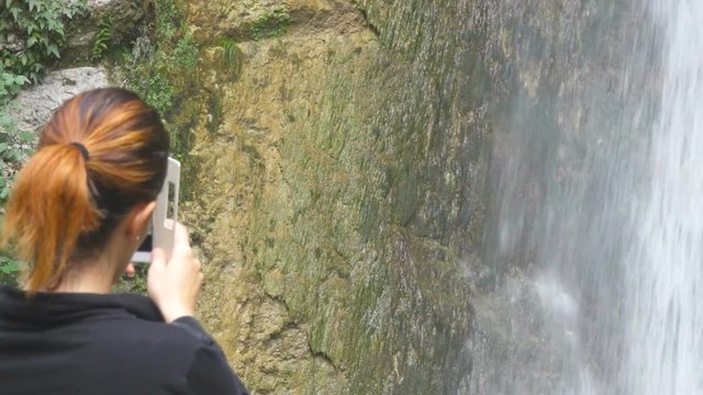Woman hiker taking photo of a waterfall with her smartphone