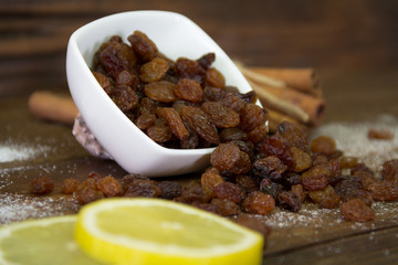 Raisins spilled from a bowl on the wooden table. Lemon and cinnamon