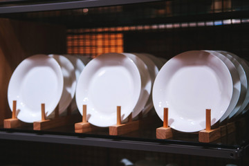 White plates on a wooden stand. Ceramic white plates on wooden shelf in a row closeup