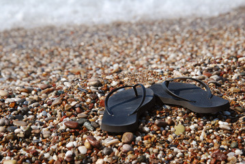 Black Flip Flops on the Beach, with Sea on background. Holliday Concept. summer. vacation.