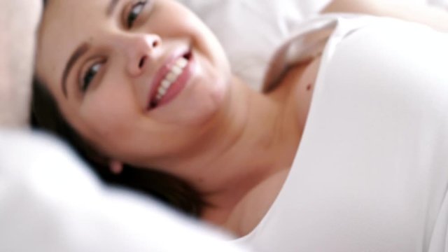 Close up view of Pleased pregnant woman lying on bed together with her husband while man touching her tummy and kissing her